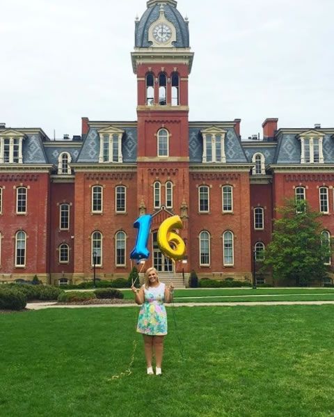 Holding "one" and "six" balloons in front of Woodburn Hall