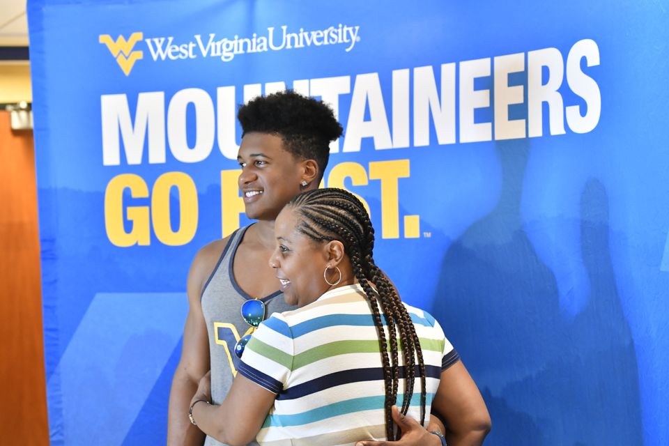 A mother and son pose in front of a Mountaineers Go First banner