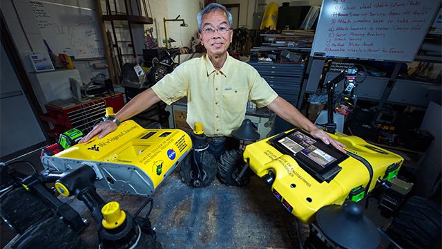 A WVU professor posing with two WVU-branded robots