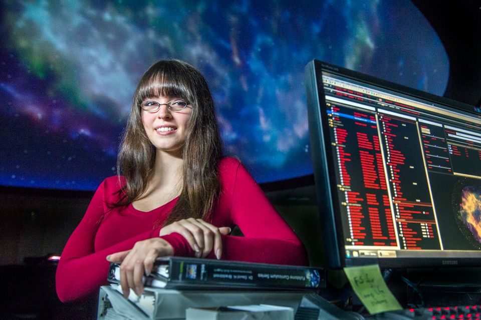 A student smiles in front of a projection of stars in the planetarium